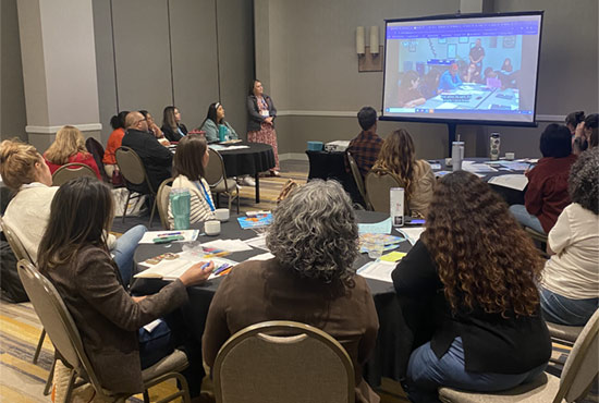 A woman in a dress presenting to a group of educators during a CRLP learning event